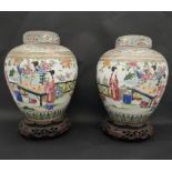A pair of Qing period Famille Rose lidded ginger jars on carved and pierced hardwood stands.