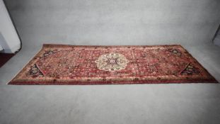 A Persian carpet with central floral medallion on madder ground within naturalistic floral spandrels