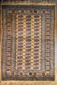 A Bokhara style rug with repeating gul motifs on a sand ground within stylised flowerhead multiple