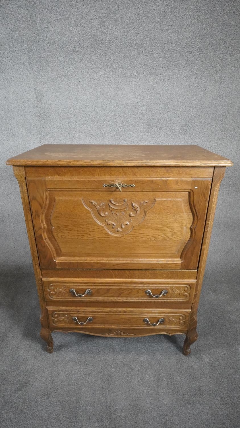 A Continental light oak drinks cabinet with carved fall above two drawers on cabriole supports. H.