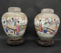 A pair of Qing period Famille Rose lidded ginger jars on carved and pierced hardwood stands.