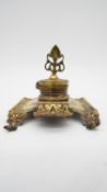 An antique brass hinged lidded inkwell with two pen rests. The inkwell has a stylised foliate and
