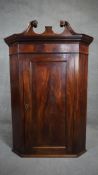 A Georgian flame mahogany hanging corner cabinet with swan neck pediment above fielded panel door