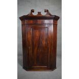 A Georgian flame mahogany hanging corner cabinet with swan neck pediment above fielded panel door