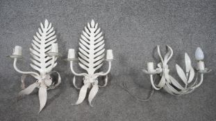 A pair of white painted twin branch wall candelabras with fern and flowerhead decoration along
