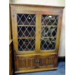 AN OAK LEADED AND GLAZERS BOOKCASE WITH LINENFOLD DOORS TO THE BASE H-136.5 W-97 CM