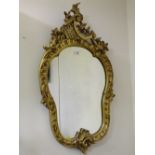 A DECORATIVE GILTWOOD CARVED WALL MIRROR, the shaped glass set within a carved Rococo style frame