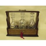 A VINTAGE OAK THREE BOTTLE TANTALUS WITH SEVEN DECANTER LABELS