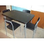 A BLACK DINING TABLE AND FOUR STACKABLE CHAIRS