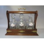 A TWENTIETH CENTURY MAHOGANY THREE DECANTER TANTALUS, with three ceramic decanter labels, with