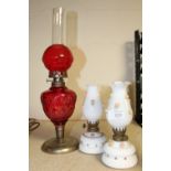 A PAIR OF SMALL OPAQUE GLASS OIL LAMPS WITH FLORAL DETAIL TOGETHER WITH A RED GLASS EXAMPLE (3)