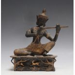 A TIBETAN TYPE BRONZE FIGURE OF A DEITY PLAYING A FLUTE, sat upon a forest with deer being chased by