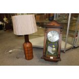 A TURNED WOODEN TABLE LAMP TOGETHER WITH A REPRODUCTION LEGEND WALL CLOCK, LAMP HEIGHT WITH SHADE 68