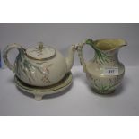 A BELLEEK TEAPOT, A BELLEEK JUG BOTH WITH BLACK MARKS TO BASE AND A TEAPOT STAND, NO MARK