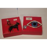 BUTLER AND WILSON TWO BOXED BROOCHES, ONE A LARGE BLUE EYE THE OTHER A LADY AND DOG