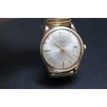 A VINTAGE J W BENSON GOLD DATE WATCH, probably 9 carat, on expandable plated bracelet,