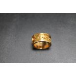 AN UNMARKED YELLOW METAL BAND, decorated text all around, approx weight 8.4g, ring size K 1/2
