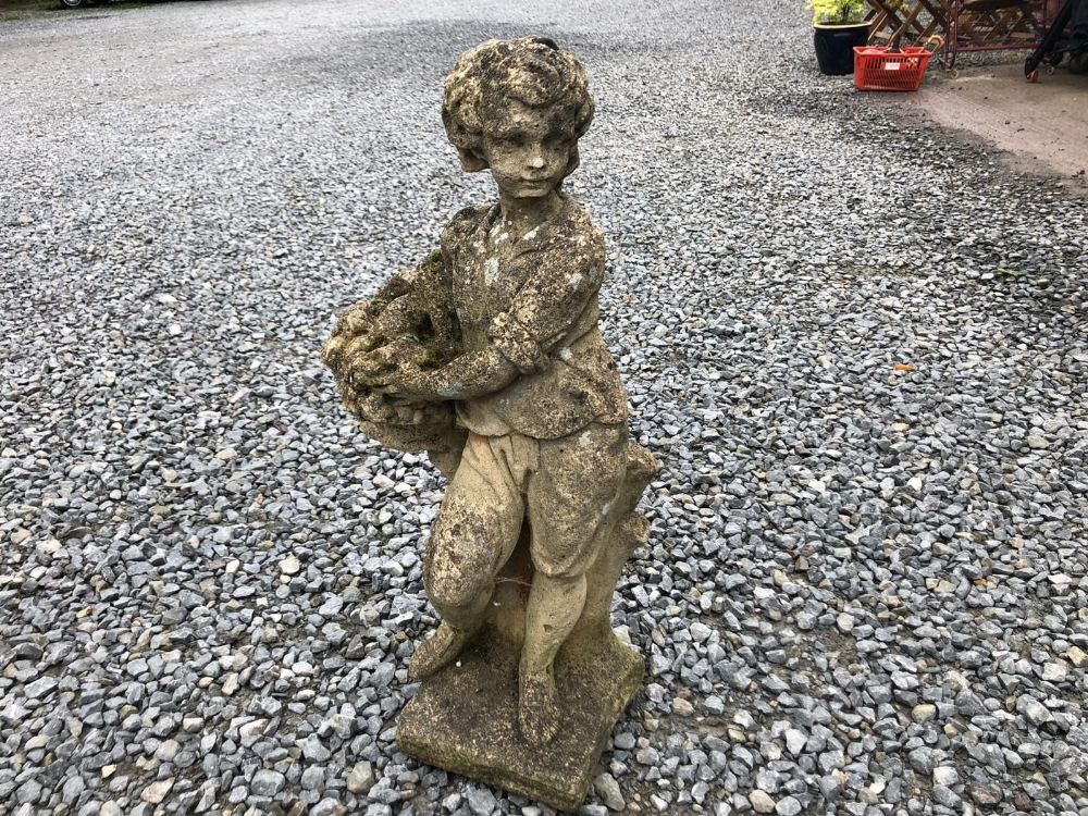 A WEATHERED RECONSTITUTED STONE FIGURE 'SUMMER', modelled as a boy carrying a basket of flowers.