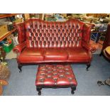 AN OXBLOOD LEATHER WINGBACK THREE SEATER SETTEE W-180 CM TOGETHER WITH A OXBLOOD LEATHER FOOTSTOOL