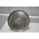 AN ISLAMIC WHITE METAL CIRCULAR TRAY OF HAND RAISED FORM WITH A CENTRAL CARTOUCHE OF SCRIPT, D 22