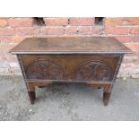 AN 18TH CENTURY OAK SINGLE PLANK COFFER, the typical hinged lid over a later carved front, raised on