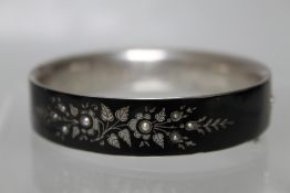 A VICTORIAN SILVER AND ENAMEL MOURNING BANGLE, with pique inlay and seed pearl embellishment, the