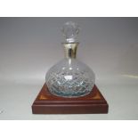 A SILVER COLLARED CUT GLASS DECANTER AND STAND, the silver collar having engraved dedication, the