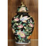 AN ORIENTAL LIDDED VASE DECORATED ON BLACK GROUND WITH BIRDS AND FLOWERS AND HAVING AN OVAL
