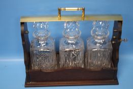 A REPRODUCTION THREE BOTTLE TANTALUS, one decanter signed 'Stuart', mahogany base with brass locking