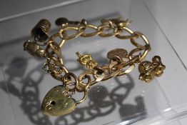 A YELLOW METAL CHARM BRACELET, unmarked bracelet, gold plated clasp, with seven fixed charms and two