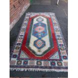 A VINTAGE WOOLLEN RUG ON A MAINLY RED GROUND 315 x 172 cm