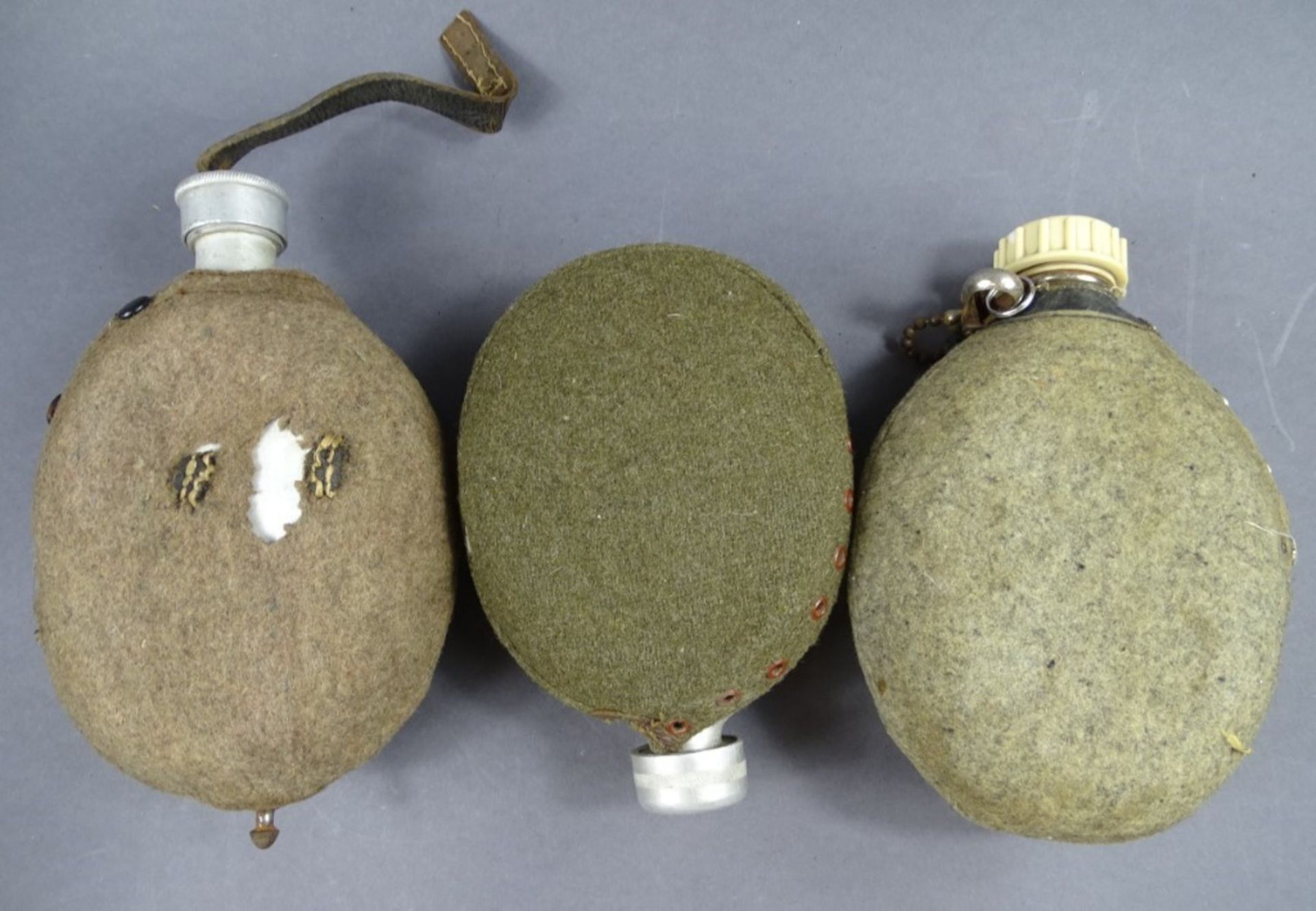 3 Feldflaschen in Filzhülle, Filz löchrig und fleckig, Lederteile rissig, Metall z.T. rostig