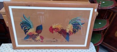 A framed embroidery of two fighting cocks.