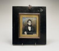 An early to mid 19th-century miniature portrait of a young gentleman seated by a table with books