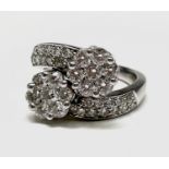 An 18ct white gold and diamond flowerhead crossover ring, 7.9g. Ring size O. Total diamond weight