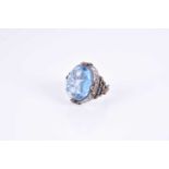 An unusual silver and blue glass ring,set with an oval blue glass cabochon, of stylised naturalistic