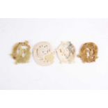 Four Chinese jade amulets, Warring States period, each carved as a coiling dragon, the stones from