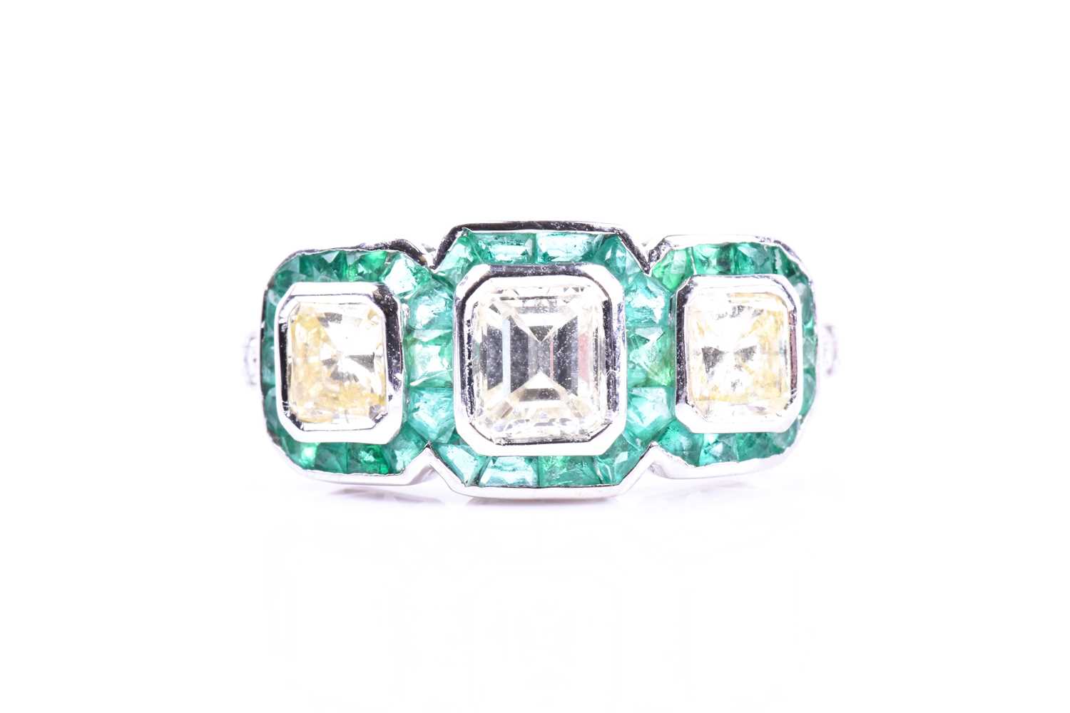 A diamond and emerald ring, set with an emerald-cut diamond flanked with two mixed square-cut
