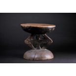 An African carved wood stool, with a slightly dished circular top, with cruciform support on a domed