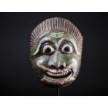 An Indonesian carved and painted wood mask, with linear coiffure, the face painted in white, green