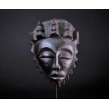 A Baule female mask, Ivory Coast, with stylised coiffure, cross form scarification marks to the