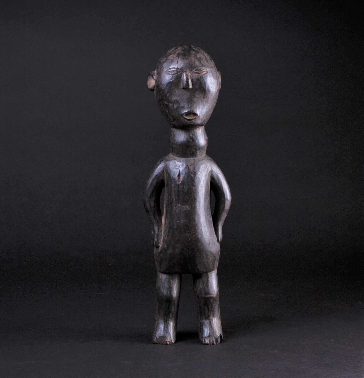 An East African carved wood standing figure of a man, Possibly Kamba, Kenya, his hands resting