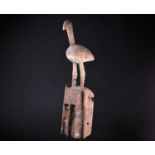 A Dogon mask, Mali, surmounted by a large bird above a metal hook, the mask painted with white,