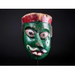 An Indonesian carved and painted wood sickness type mask, with distorted nose and mouth, pierced