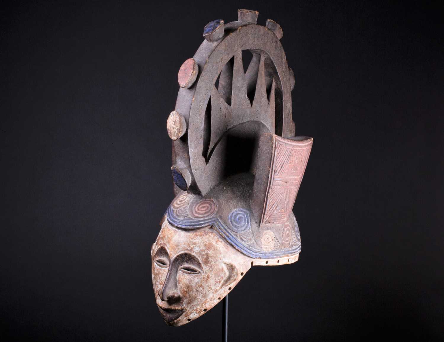 An Igbo Maiden Spirit mask, Nigeria, in red, blue and white pigment, the edges pierced with holes,