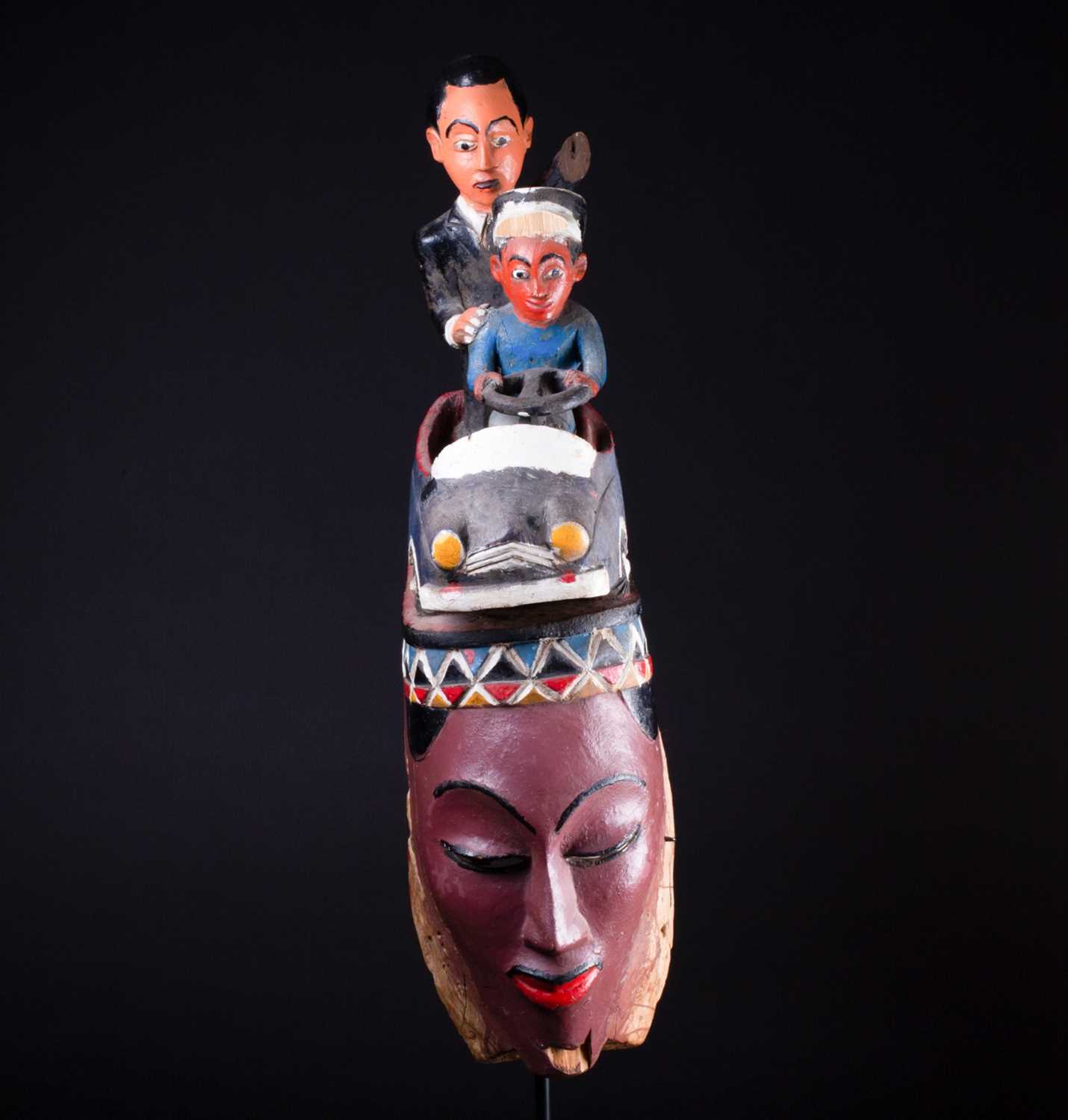 A Colon mask, Nigeria, the female mask painted in polychrome, surmounted by a car with a standing