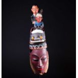 A Colon mask, Nigeria, the female mask painted in polychrome, surmounted by a car with a standing