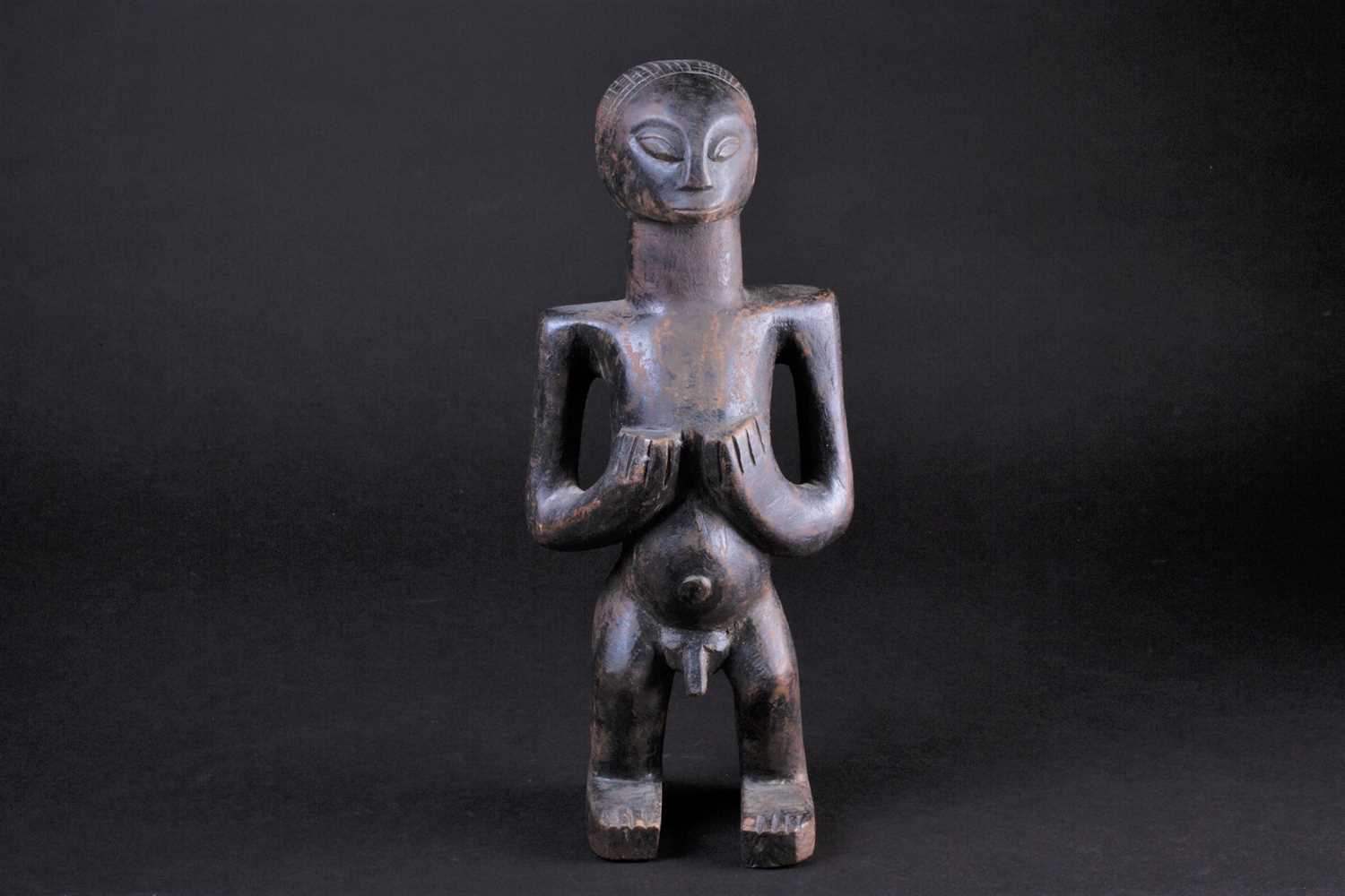 An East African standing male fertility figure, with cross hatched coiffure, his hands turned up