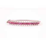 A ruby and diamond half hoop bangle; the front set with sixteen oval cut rubies, with a divided band