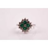 An emerald and diamond cluster ring; the five stone central cluster within a border of tiered